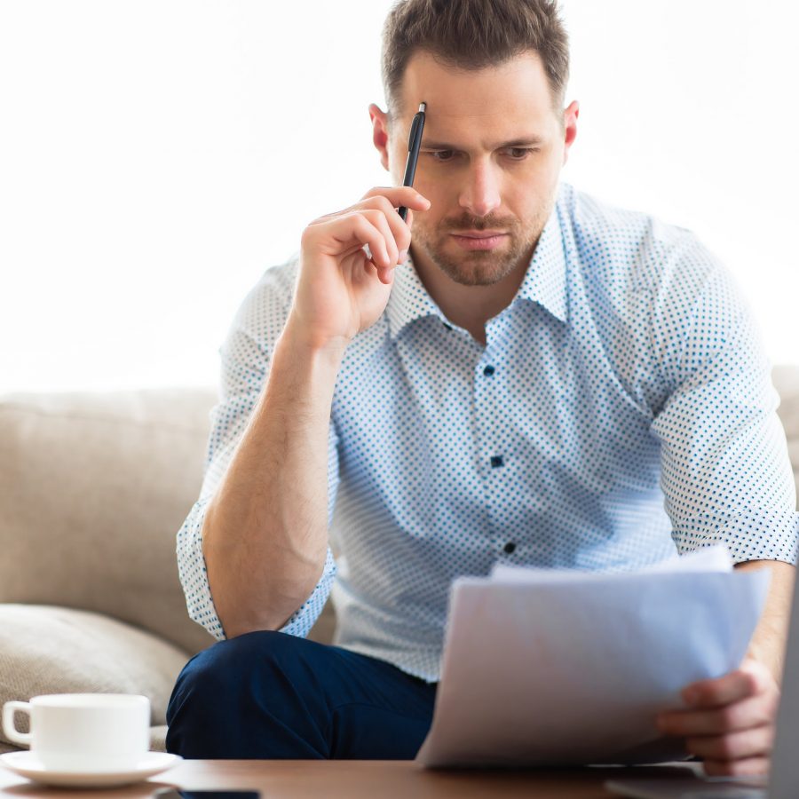 Pensive young man sitting at desk, looking at documents